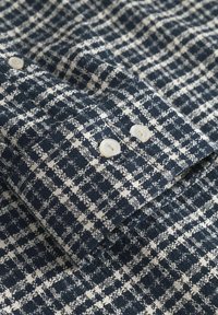 Navy- und weiß kariertes Stoffhemd mit strukturiertem Gewebe, zwei cremefarbenen Knöpfen an den Ärmeln und einem klassischen Kragendesign.