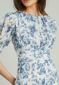 Abito floreale in tessuto bianco e blu, con scollatura arricciata, maniche a sbuffo corte e vita aderente con pieghe.
