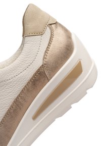 Gros plan sur le talon d'une basket blanche et beige avec cuir texturé, bord supérieur en daim, détail latéral métallique et semelle blanche épaisse.