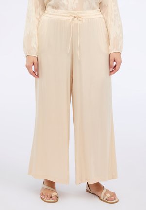 Pantalons larges en tissu beige clair et doux avec une taille à cordon. Ils présentent une coupe décontractée et une texture lisse pour le confort.