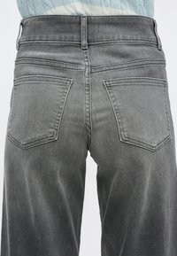 Sive kavbojke iz jeansa z visokim pasom, s dvema zadnjima žepoma in subtilnim šivom. Tkanina je mehka in rahlo obrabljena.