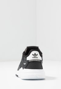 Baskets de sport noires avec tige en mesh, accents en daim, semelle blanche et logo Adidas sur le talon. Dotées d'un col rembourré et d'une surface texturée.