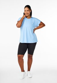 Light blue athletic top with short sleeves, paired with black cycling shorts. Model wears white sneakers. Simple design and fit.
