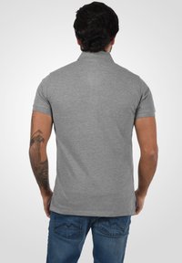 Grå bomulds polo skjorte med krave og korte ærmer, parret med blå denim jeans, der viser en tatovering på venstre arm.