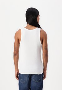 Weißes Baumwoll-Trägershirt mit gerippter Struktur, breiten Trägern und runder Ausschnitt, kombiniert mit blauen Jeans.
