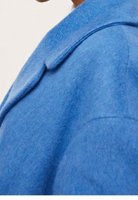 Abrigo de lana azul con un cuello estructurado y mangas ligeramente holgadas, que presenta una textura suave y una silueta limpia.