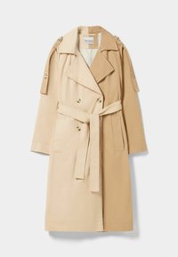 Beżowy płaszcz trench z podwójnym zapięciem, z paskiem w talii, pagonami na ramionach i bocznymi kieszeniami, wykonany z lekkiego materiału.