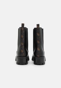 Botines negros con un acabado texturizado, paneles laterales elásticos y una correa decorativa con el logo marrón en la parte posterior. Suelas de goma gruesas para tracción.