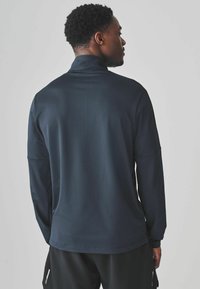Camiseta deportiva de manga larga en color navy con cuello alto, textura suave y detalles de costura sutil, vista desde la parte de atrás.