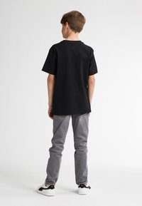 Zwarte katoen t-shirt met korte mouwen, gecombineerd met grijze denim broek en witte sneakers met zwarte accenten. Zichtbare achterkant.