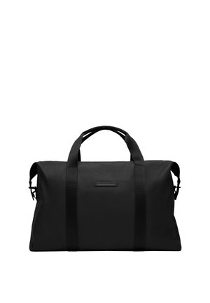 Sac de sport noir en tissu résistant, de forme rectangulaire, avec des poignées épaisses et un design minimaliste agrémenté d'un petit détail.