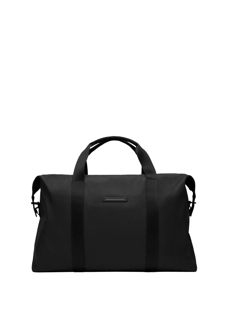 Sac de sport noir en tissu résistant, de forme rectangulaire, avec des poignées épaisses et un design minimaliste agrémenté d'un petit détail. 
