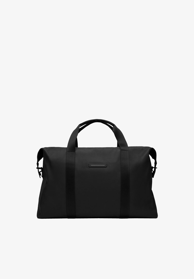 Sac de sport noir en tissu résistant, de forme rectangulaire, avec des poignées épaisses et un design minimaliste agrémenté d'un petit détail.