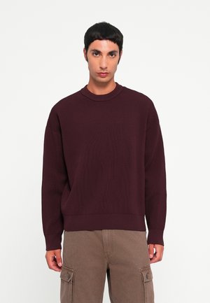 Bordeaux ribbelgebreide trui met een ronde halslijn en een dropped shoulder-stijl, gecombineerd met bruine cargobroek met zijzakken.