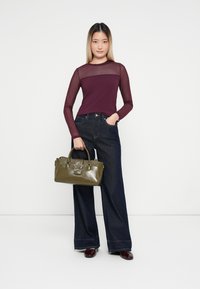 Vinröd långärmad topp med genomskinliga ärmar, kombinerad med vida jeans i mörk denim. Håller en olivgrön handväska med en stjärndetalj.