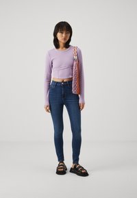 Svijetloplavi dugi rukavi skraćeni top u kombinaciji s tamnoplavim uskim trapericama i crnim platformama. Outfit uključuje šarenu tkanu torbu.