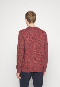 Maglione lavorato a maglia in tonalità rosso e nero, con collo rotondo, maniche lunghe e polsini e orlo a coste. Tessuto morbido con motivo melangiato.