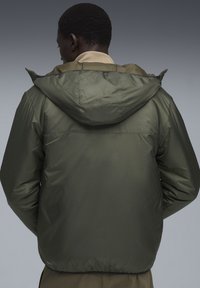 Jachetă căptușită de culoare verde măslin, cu glugă, textură netedă, manșete elastice și talie elastică. Design simplu și funcțional.