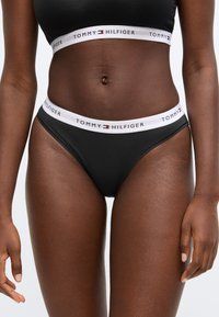 Černé bavlněné bikiny s bílým elastickým páskem s nápisem "TOMMY HILFIGER". Hladká textury a přiléhavý střih.