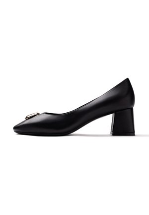 Zapato de tacón medio de cuero negro con detalle de hebilla cuadrada en la punta puntiaguda, mostrado sobre un fondo blanco mirando hacia la izquierda.