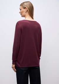Bordeaux lange mouw sweater met een brede halslijn en geribde manchetten. Zachte textuur, relaxte pasvorm en een rechte zoom. Gstyled met donkere jeans.
