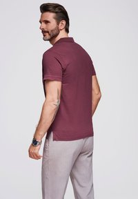 Polo a maniche corte di colore bordeaux con colletto piatto, abbinato a pantaloni grigi chiari. Tessuto morbido e vestibilità casual.