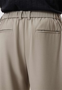 Elastische taillebroek van lichtbeige stof, voorzien van zijzakken met een soepele textuur en een op maat gemaakte uitstraling voor een getailleerd uiterlijk.