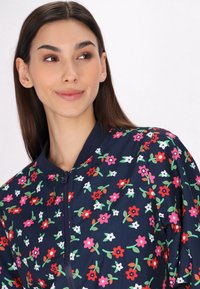 Bloemen bomberjack van navy stof, met bloemen in meerdere kleuren zoals rood, roze en wit. Ritsluiting en geribbelde kraag.