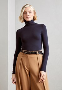 Top de tortuga azul marino combinado con pantalones de pierna ancha de cintura alta en marrón claro. Presenta un cinturón tejido negro con una hebilla plateada. Textura de tela suave.