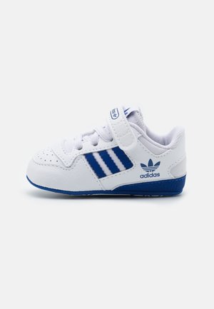 Baskets blanches Adidas pour tout-petit avec des bandes bleues, semelle bleue et bride velcro sur fond blanc uni.