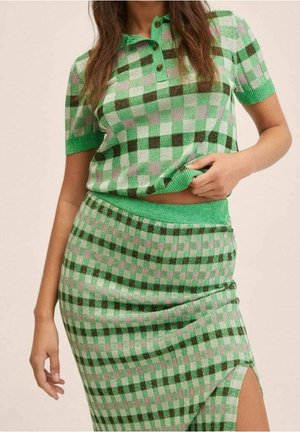 Donna che indossa un top polo in maglia a quadri verdi, rosa e scuri e una gonna a vita alta abbinata con uno spacco laterale.