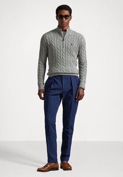 Sweater cinzento em malha trançada com meio fecho, combinado com calças náuticas risca de giz. Sapatos de pele castanha completam o conjunto.