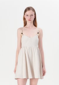 Beige pellava-mekko, jossa on istuva yläosa, levenevä helma ja ohuet hihnat, joissa on koristeellisia helmiä eri väreissä. Sileä pinta ja yksinkertainen muotoilu.