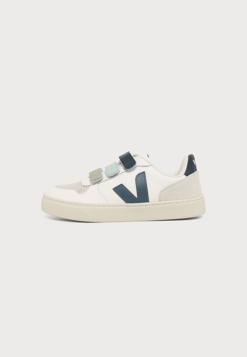 Baskets blanches avec embout beige, trois bandes velcro en vert et bleu, logo "V" bleu foncé et semelle crème sur fond uni.