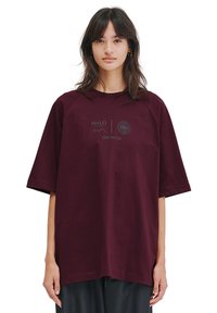 Burgunderfärgad oversized t-shirt i bomull, med raglanärmar och två framsidor med logotyper. Slät textur med avslappnad passform.