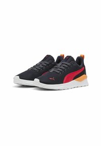 Chaussures de sport en mesh noir avec des accents rouges et orange, semelle blanche et lacets gris. Présentent un col rembourré et un panneau latéral texturé.