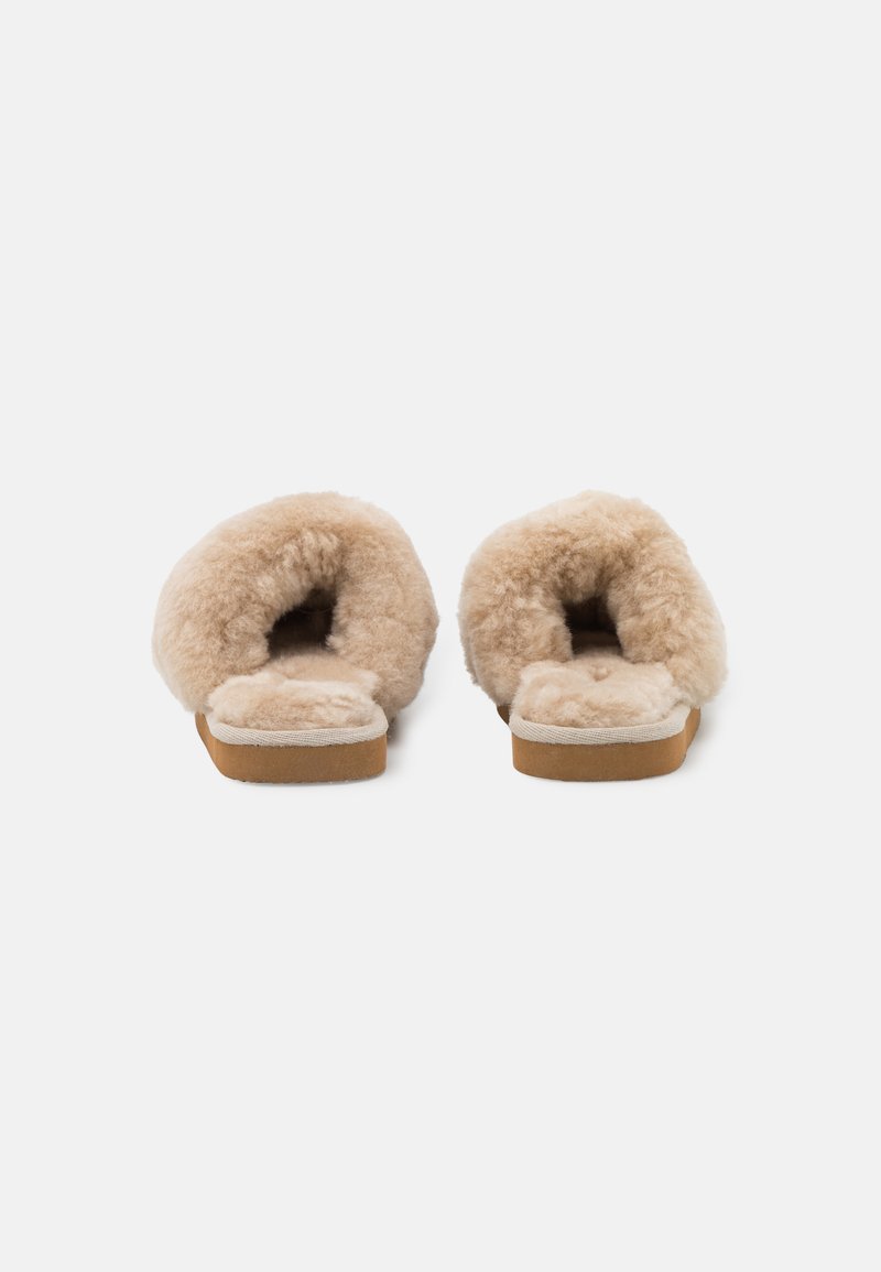 Beige Schaffellslipper mit weicher, flauschiger Textur, offenem Design an der Rückseite und einfacher Gummisohle. Keine zusätzlichen Verzierungen oder Muster.