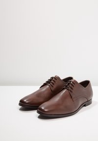 Bruna läderskor för fest med en slät yta, rundade tår, snörning och subtila sömnadsdetaljer. Lågt profilerade gummisålar.