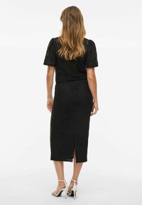 Conjunto de dos piezas de ganchillo negro que incluye una blusa ajustada con mangas cortas abullonadas y una falda midi con una abertura, acompañada de tacones crema con tiras.