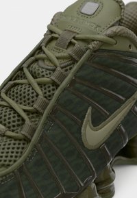 Grønne Nike Shox sneakers har en mesh-overdel med et tekstureret mønster, forstærkede snørebånd og gummisåler med karakteristisk spiral-dæmpning.