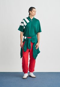 Groen T-shirt met korte mouwen met witte strepen, rode sportbroek en witte sneakers. De broek heeft strepen aan de zijkant; het shirt is in de taille geknoopt met een jas.