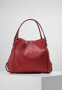 Sac à main en cuir rouge avec une forme légèrement souple, doté de doubles poignées et d'une texture subtilement granulée. Il y a une sangle latérale en détail.