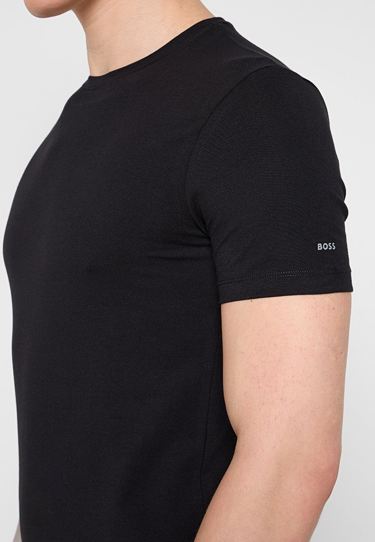 Camiseta negra de manga corta fabricada en algodón suave. Presenta un cuello redondo y un pequeño logo "BOSS" en la manga izquierda. Diseño ajustado.