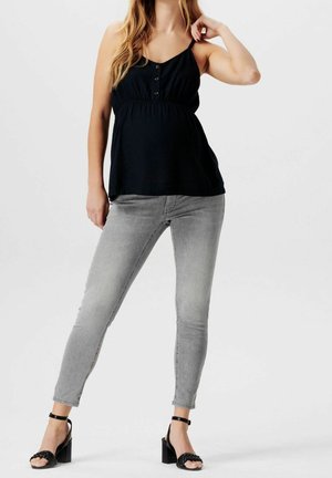 Top negro de tirantes finos con detalle de botones, de corte holgado. Combinado con jeans ajustados de mezclilla gris y sandalias negras de tacón con diseño tejido.