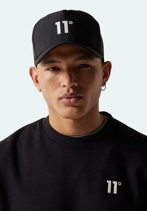 Gorra negra con el logotipo blanco "11°", llevada por una persona en un sudadera negra. Incluye un visera curva y una correa trasera ajustable.