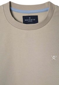 Beżowy bawełnowy t-shirt z prążkowanym okrągłym dekoltem. Posiada małe haftowane logo w dolnym prawym rogu. Metka głosi "Hackett London."