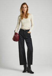 Maglione lungo a maniche lunghe di un beige chiaro a coste, jeans neri a vita alta e gamba larga, stivaletti neri con tacco e borsa a tracolla trapuntata color borgogna.