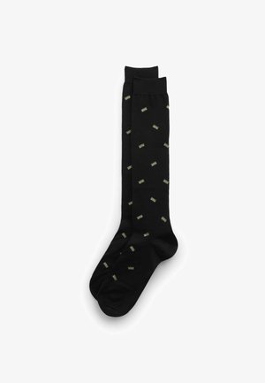 Schwarze kniehohe Socken mit einem wiederholten Muster aus grünen Dollarscheinen, gefertigt aus glattem Stoff mit weicher Textur.