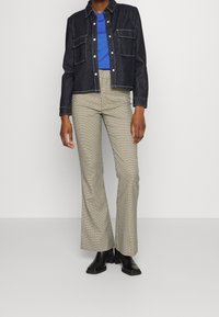 Dunkelblaue Jeansjacke mit zwei Brusttaschen, kombiniert mit hell karierten, weit geschnittenen Hosen und schwarzen Ankle-Boots. Darunter ein blauer Oberteil.