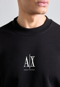 Black crewneck sweatshirt made of cotton, featuring a white embroidered logo "A|X" and "ARMANI EXCHANGE" underneath on the front.
